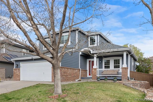 Two-story blue-gray house with brick accents, covered porch, attached garage, and a large leafless tree.