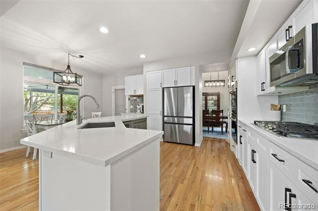 Bright white kitchen with a large island, stainless steel appliances, and warm wood floors.