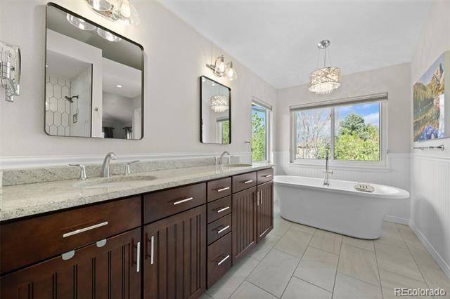 Primary bathroom with a dark double vanity and freestanding tub beneath a large window.