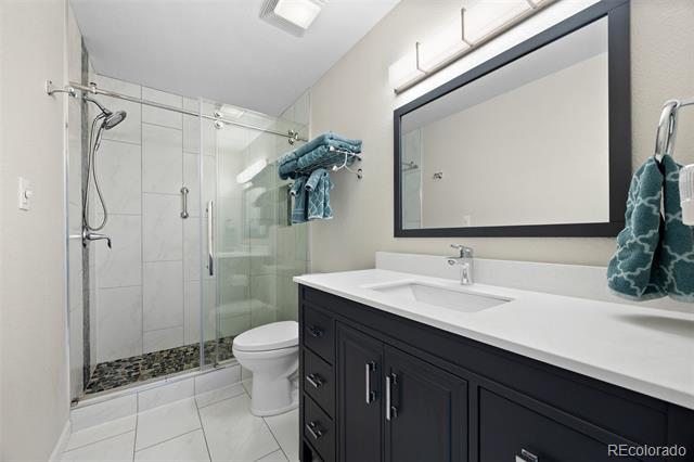 Bathroom with a glass-enclosed shower and dark vanity topped with a white countertop.