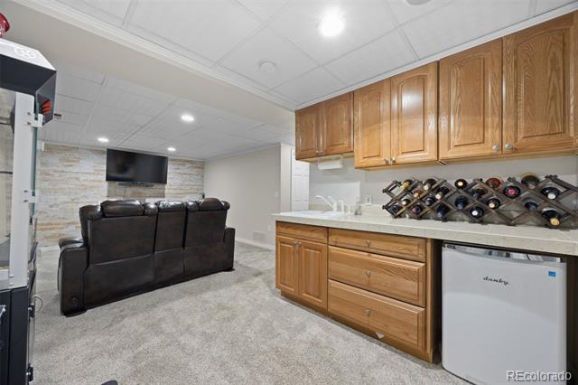 Basement wet bar and lounge with wood cabinetry, wine rack, mini fridge, and leather seating.