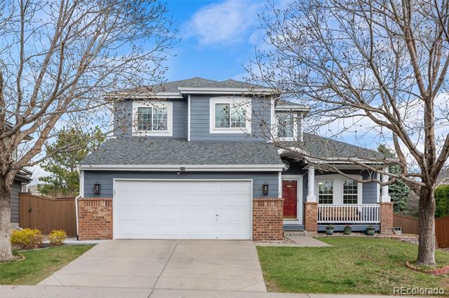Two-story blue-gray house with brick accents, white garage door, red entry door, and mature trees.