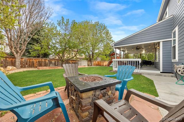 Backyard patio with a stone fire pit, blue Adirondack chairs, lawn, and covered porch.