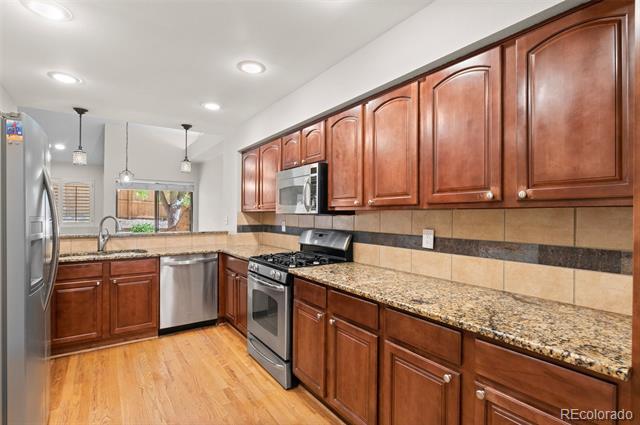 Condo kitchen with reddish-brown cabinetry, granite counters, and stainless steel appliances.