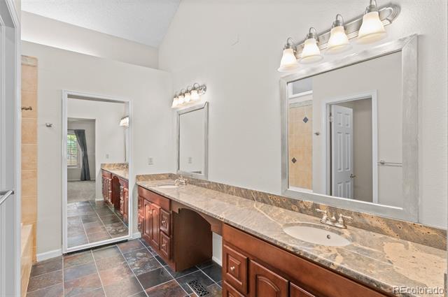 Bathroom vanity with tan stone counters, reddish-brown cabinets, two sinks, and large mirrors.
