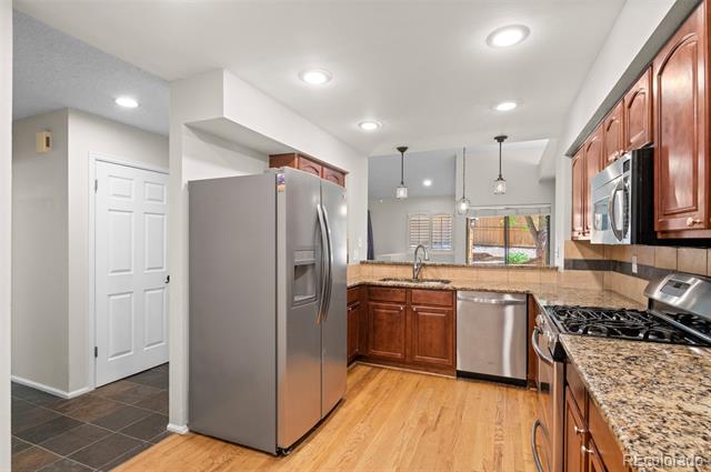Condo kitchen with wood cabinets, granite counters, stainless steel appliances, and a window overlooking greenery.
