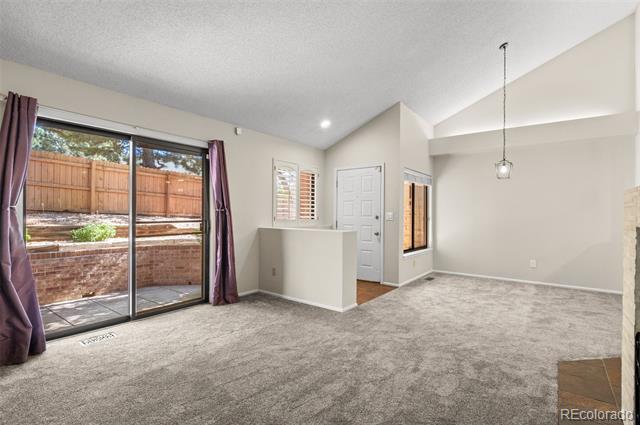 Vacant living room with vaulted ceiling, gray carpet, and sliding glass doors to a fenced patio.