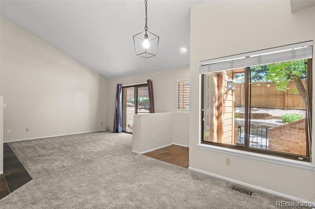 Vacant living room with gray carpet and a large window overlooking a fenced patio.