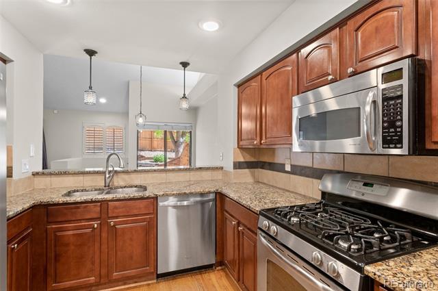 Kitchen with granite countertops, reddish wood cabinets, stainless steel appliances, and a gas range.