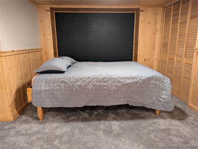 Bedroom with a gray-quilted bed, wood-paneled walls, and louvered closet doors.