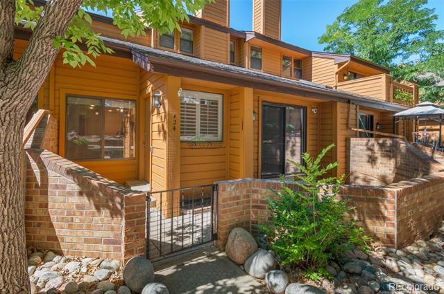 Residential unit exterior with a brick-walled patio, black metal gate, and mature trees.
