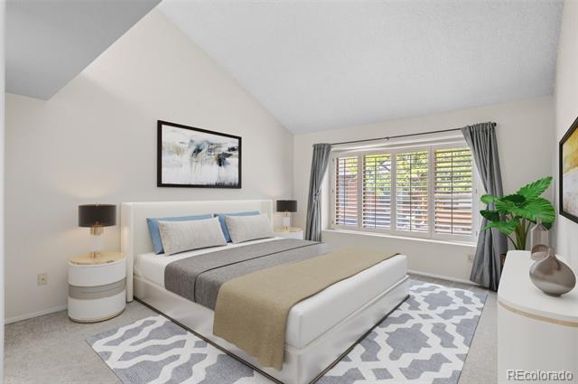 Staged bedroom with a white bed, gray bedding, patterned rug, and large shuttered window.