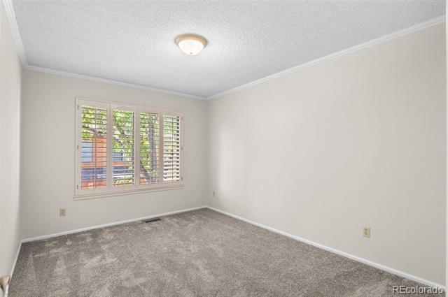 Empty bedroom with beige carpet and a window with white plantation shutters.