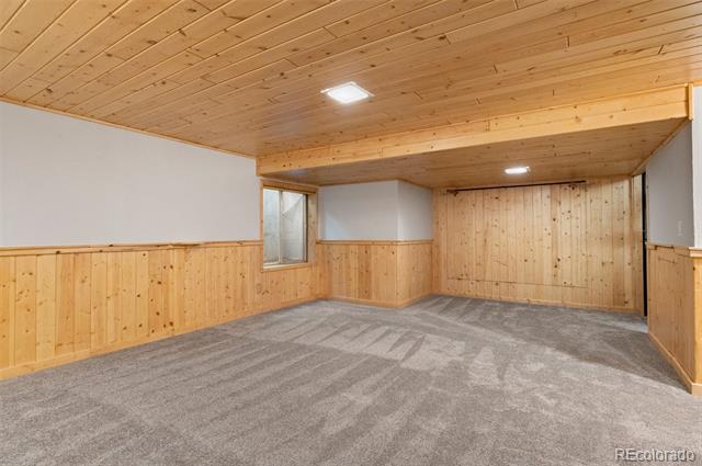 Empty carpeted room with wood-paneled walls and ceiling, a small window, and recessed lights.
