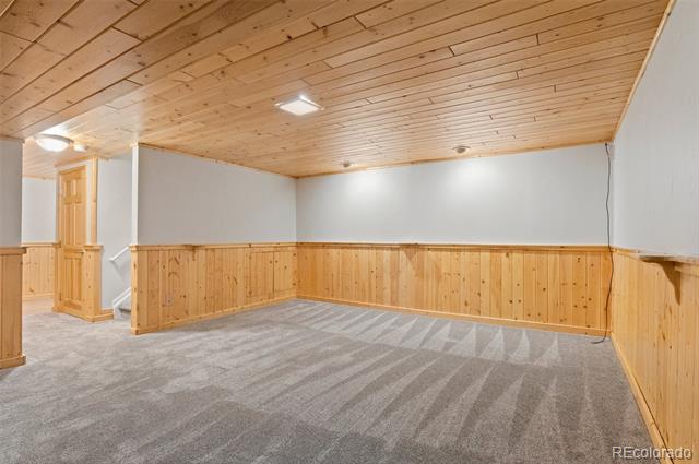 Empty lower-level room with gray carpet, wood-paneled walls, and a light wood plank ceiling.