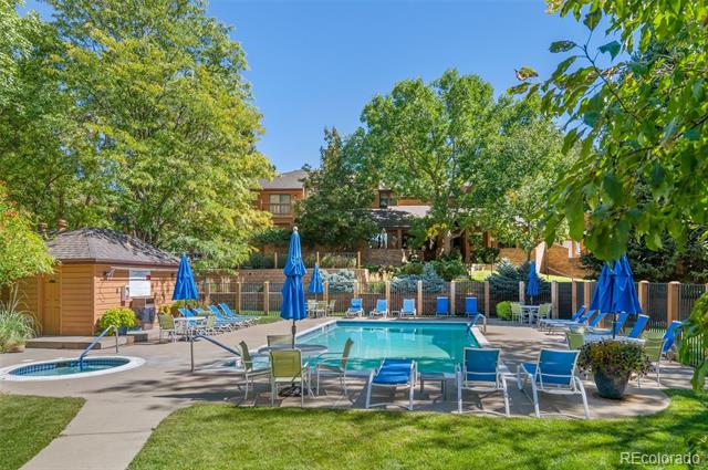 Outdoor pool and spa with blue umbrellas and lounge chairs beneath leafy trees.