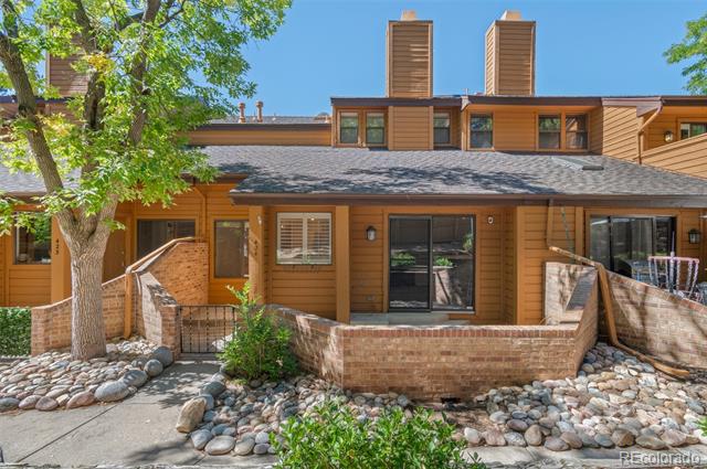 Condominium exterior with a covered entry, brick patio walls, and stone landscaping beneath a leafy tree.