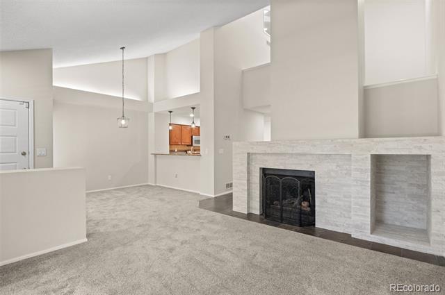 Unfurnished living room with a white stone fireplace, built-in niche, high ceilings, and gray carpet.