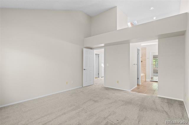 Vacant carpeted room with high ceilings, an open doorway, and a tiled area beyond.