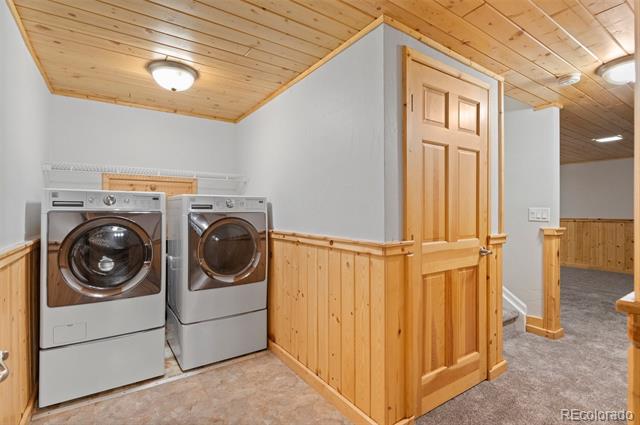 Laundry room with front-loading washer and dryer, wood ceiling, and paneled door.