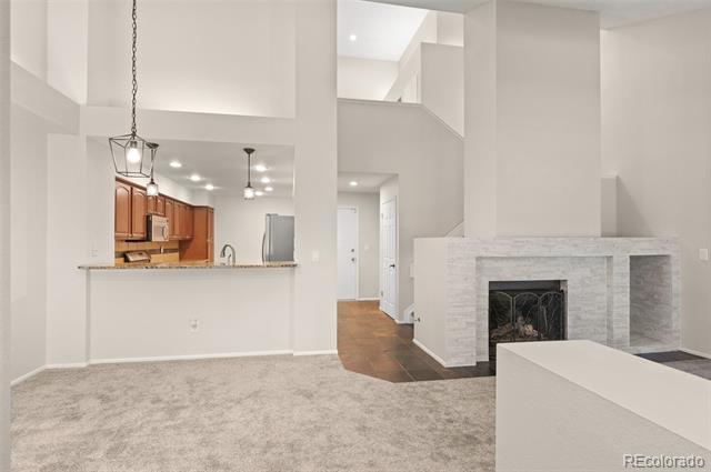 Open living area with a tiled fireplace, carpeted floor, and kitchen with wood cabinets.