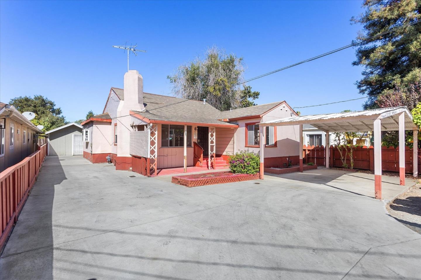 Single-story pink house with red trim, a broad paved driveway, and a covered carport.
