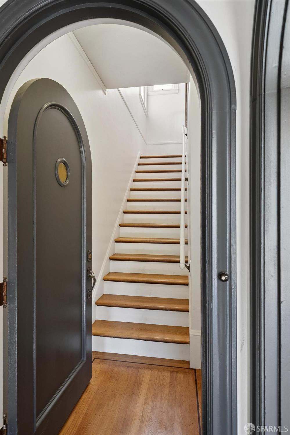 Entryway with an arched front door opening onto a wood-and-white staircase.