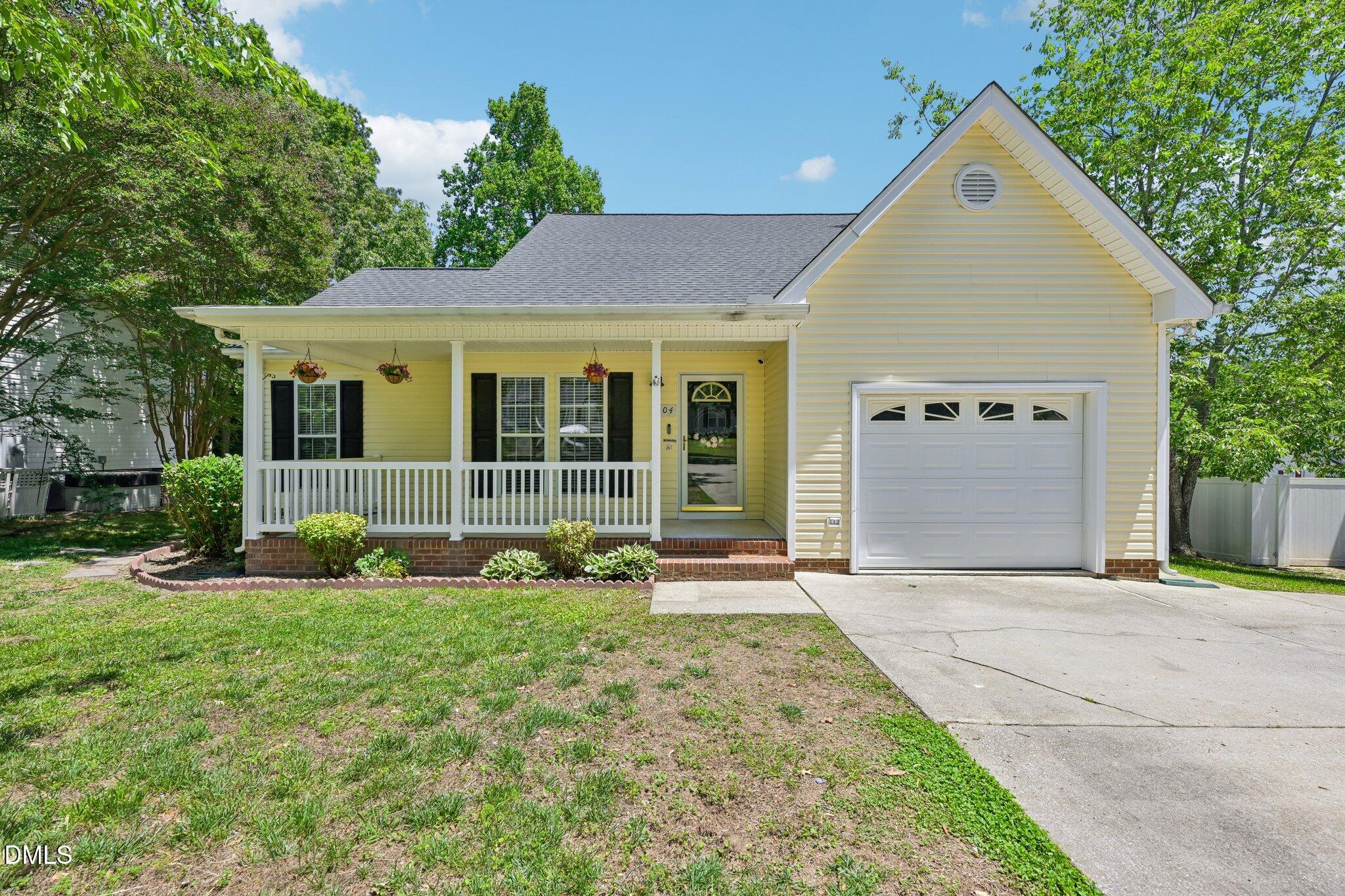 Pale yellow house with a covered porch, hanging flower baskets, and an attached garage.