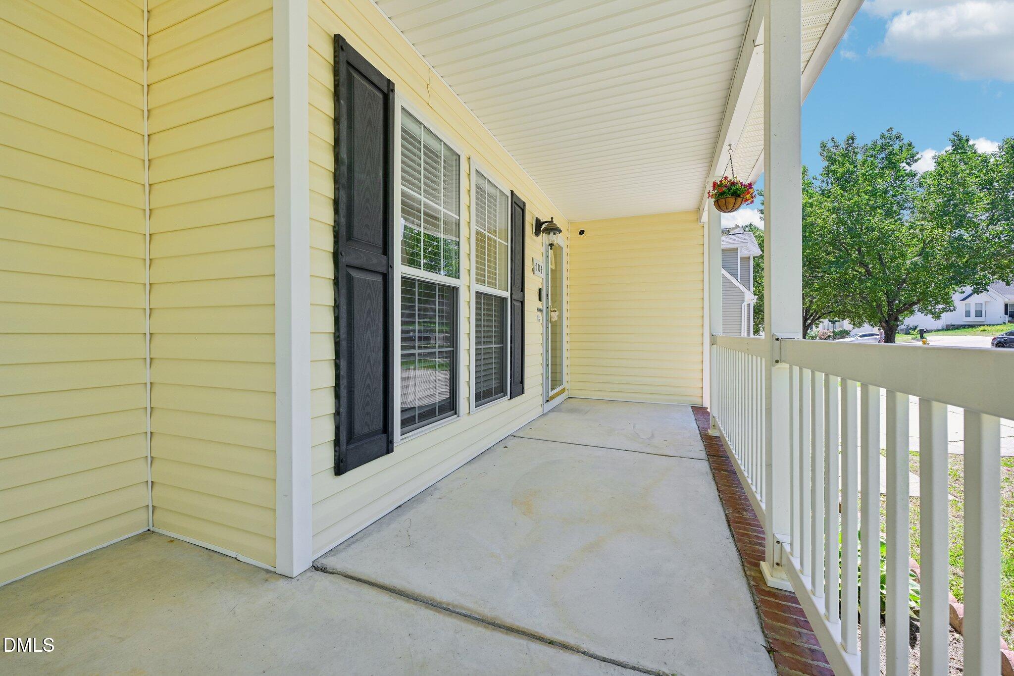 Covered porch with pale yellow siding, black shutters, white railing, and a hanging flower basket.