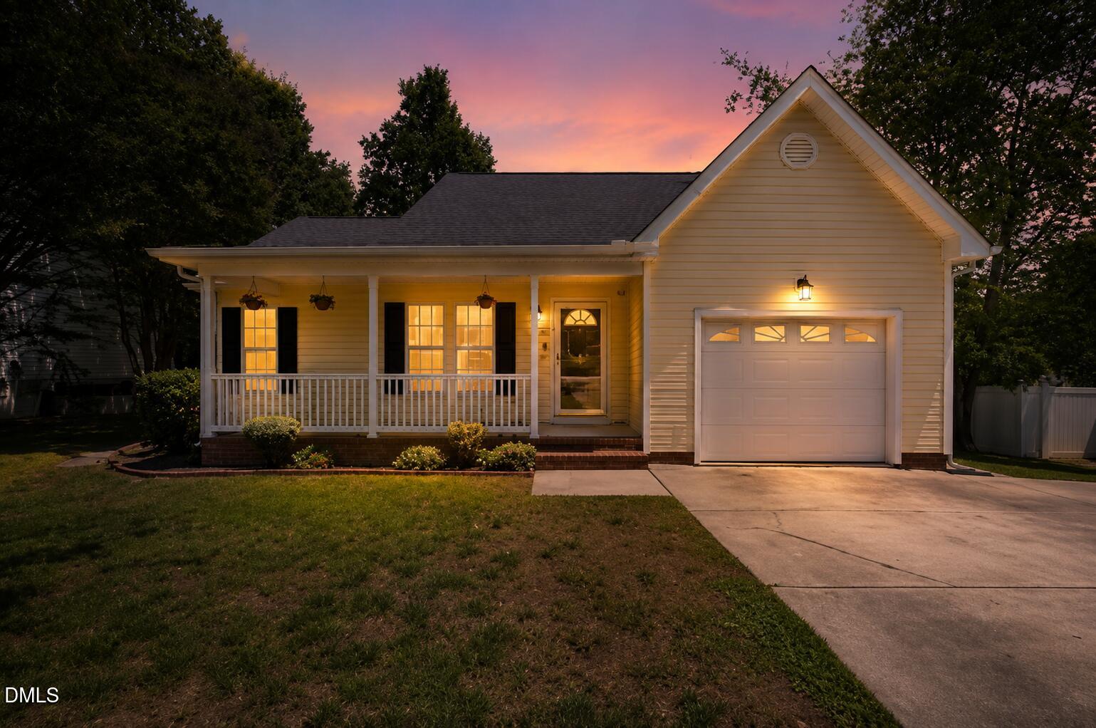 White single-story home with a covered porch and attached garage glowing at dusk.