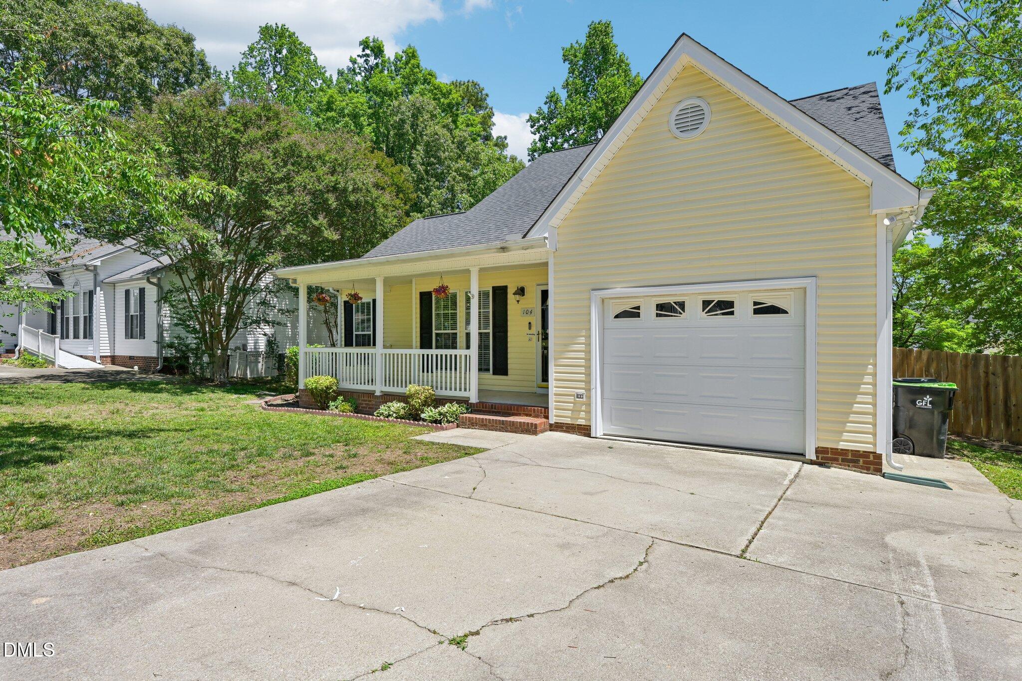 Yellow-sided home with a covered porch, attached garage, and wide concrete driveway.