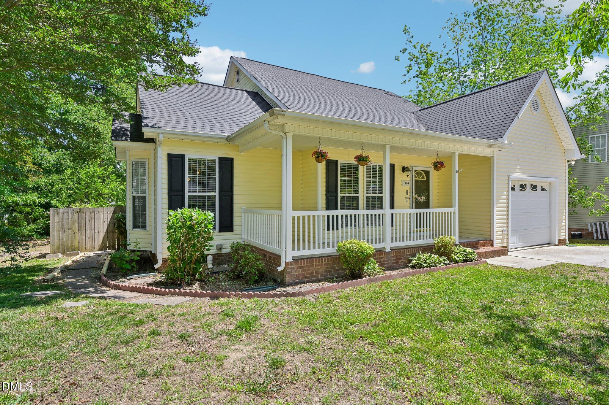 Yellow house with a covered white-railed porch, hanging flower baskets, and an attached garage.