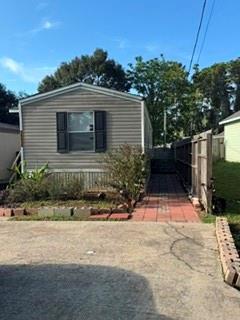 Gray-sided single-story home with dark window shutters and a brick walkway beside the driveway.