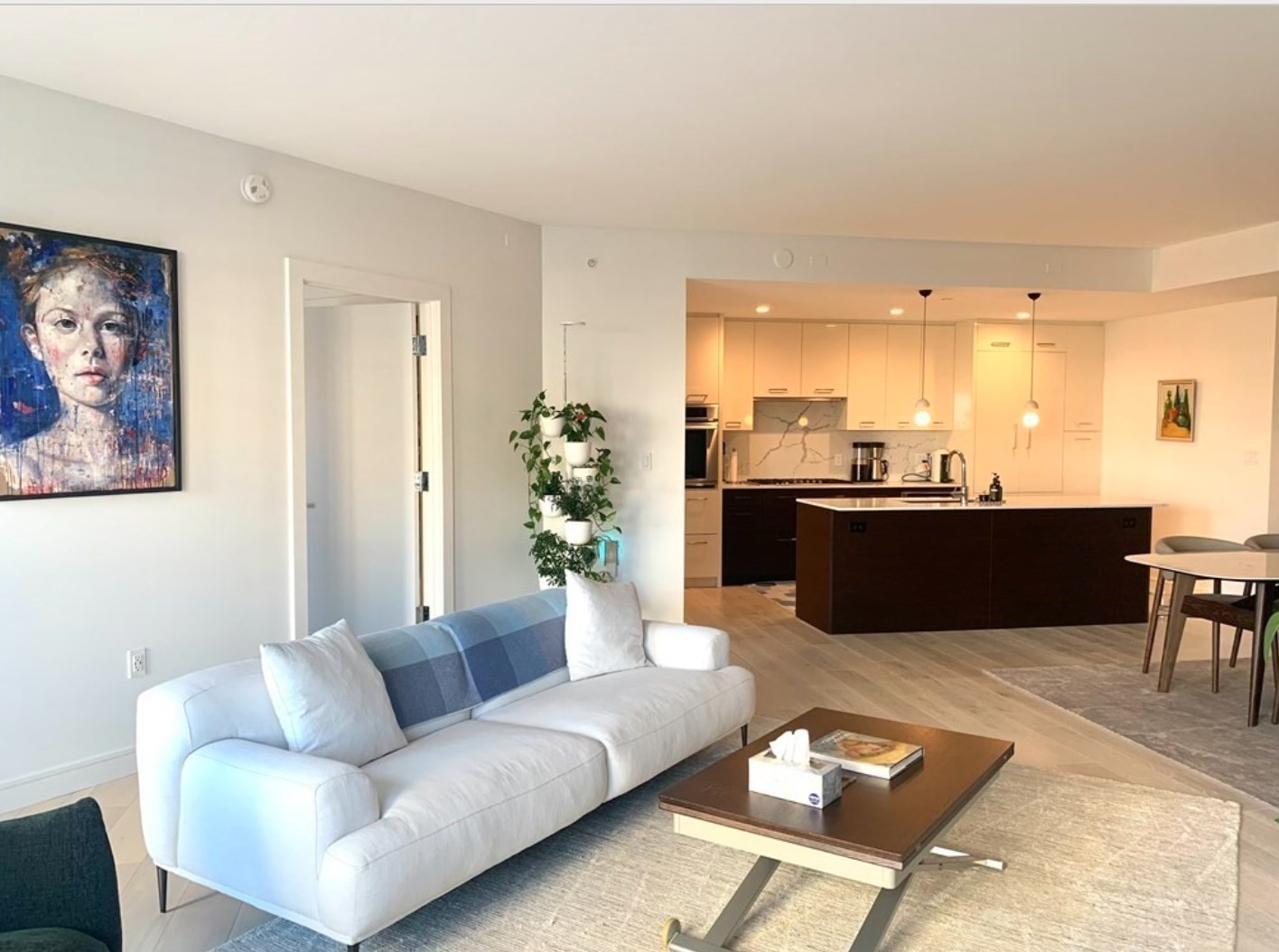Open-plan living room with a white sofa, dark kitchen island, and pendant lights.