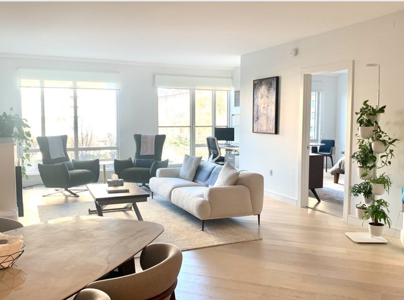 Bright living room with large windows, a white sofa, lounge chairs, and pale wood floors.