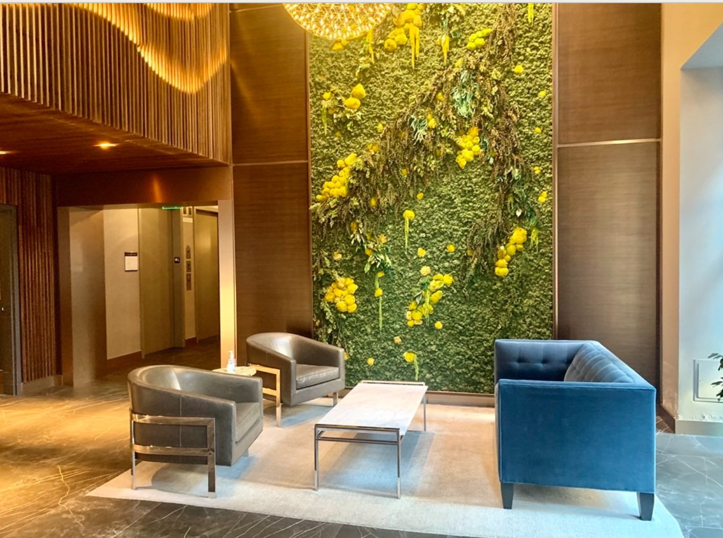 Furnished lobby with a flowered living wall, modern lounge seating, and wood-paneled elevator area.