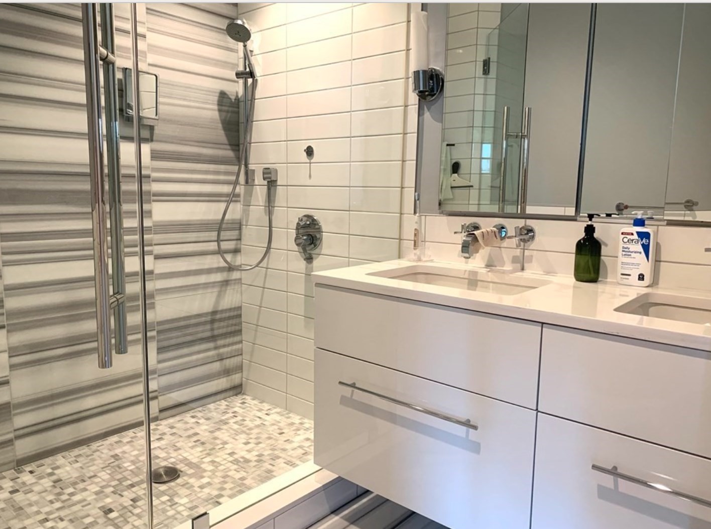 Bathroom with a glass shower, striped gray tile, mosaic floor, and white double-sink vanity.