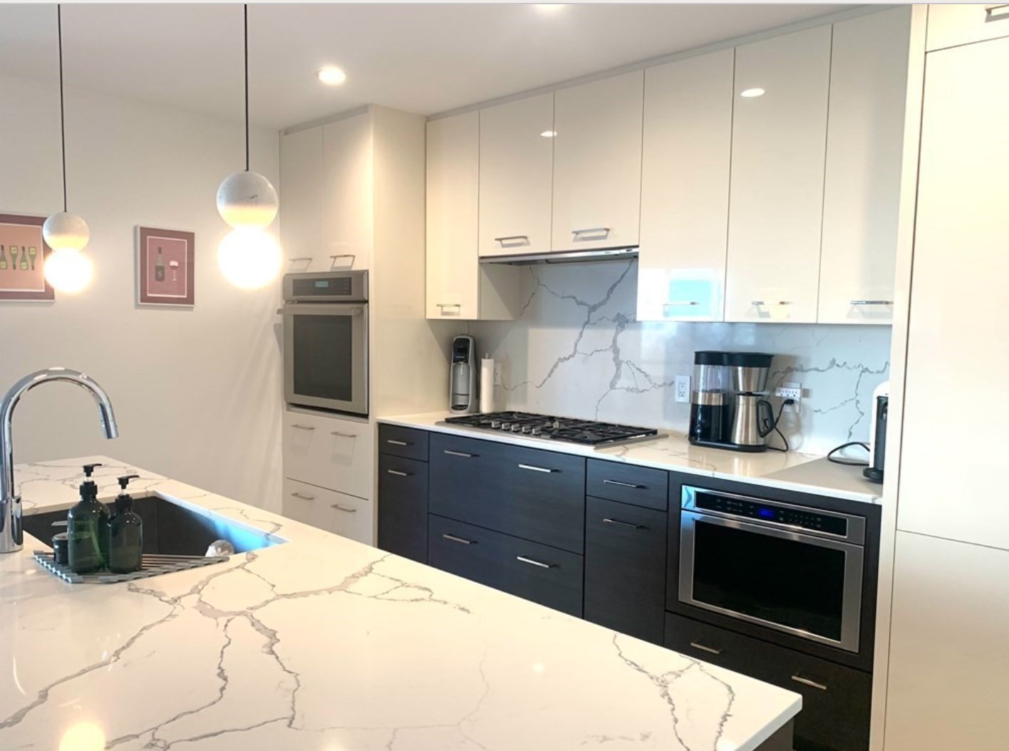 Modern kitchen with a veined marble island, white cabinets, and dark lower cabinets.