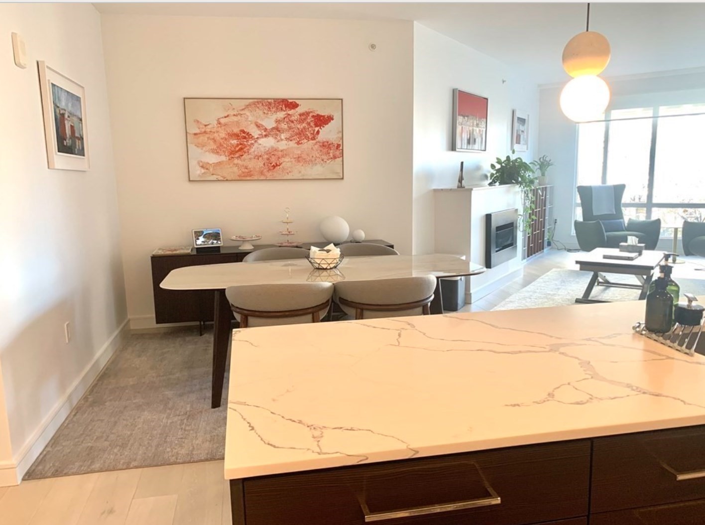 Open-plan condo kitchen with a veined stone island, dining table, fireplace, and bright windows.