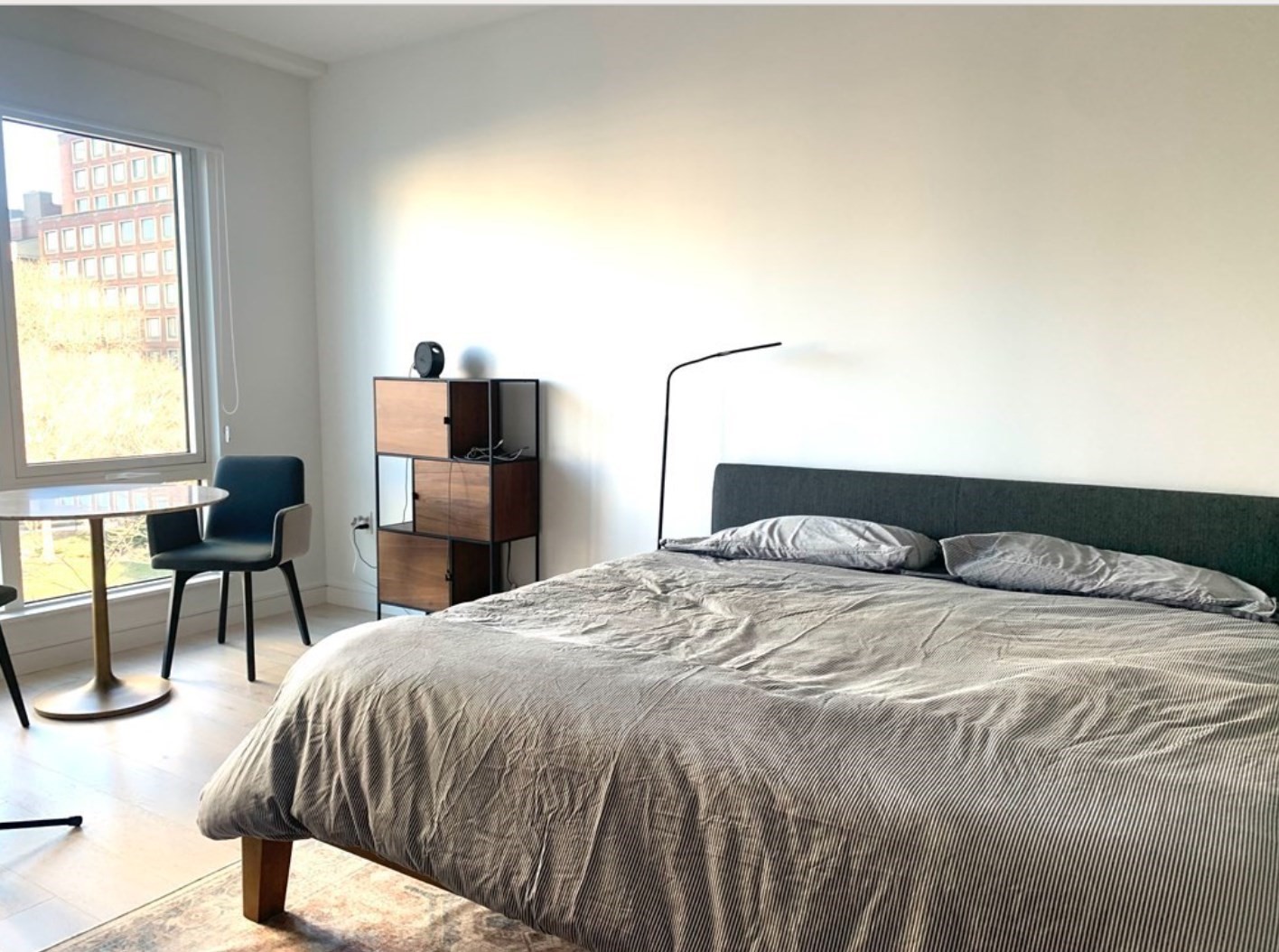 Furnished bedroom with a large bed, floor-to-ceiling window, and small seating area.