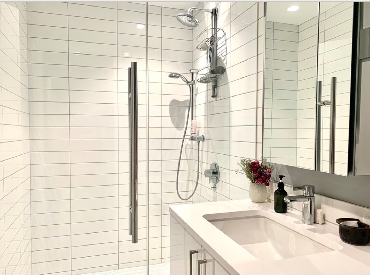 Bathroom with a glass-enclosed shower, dual showerheads, white tile, and a white vanity.