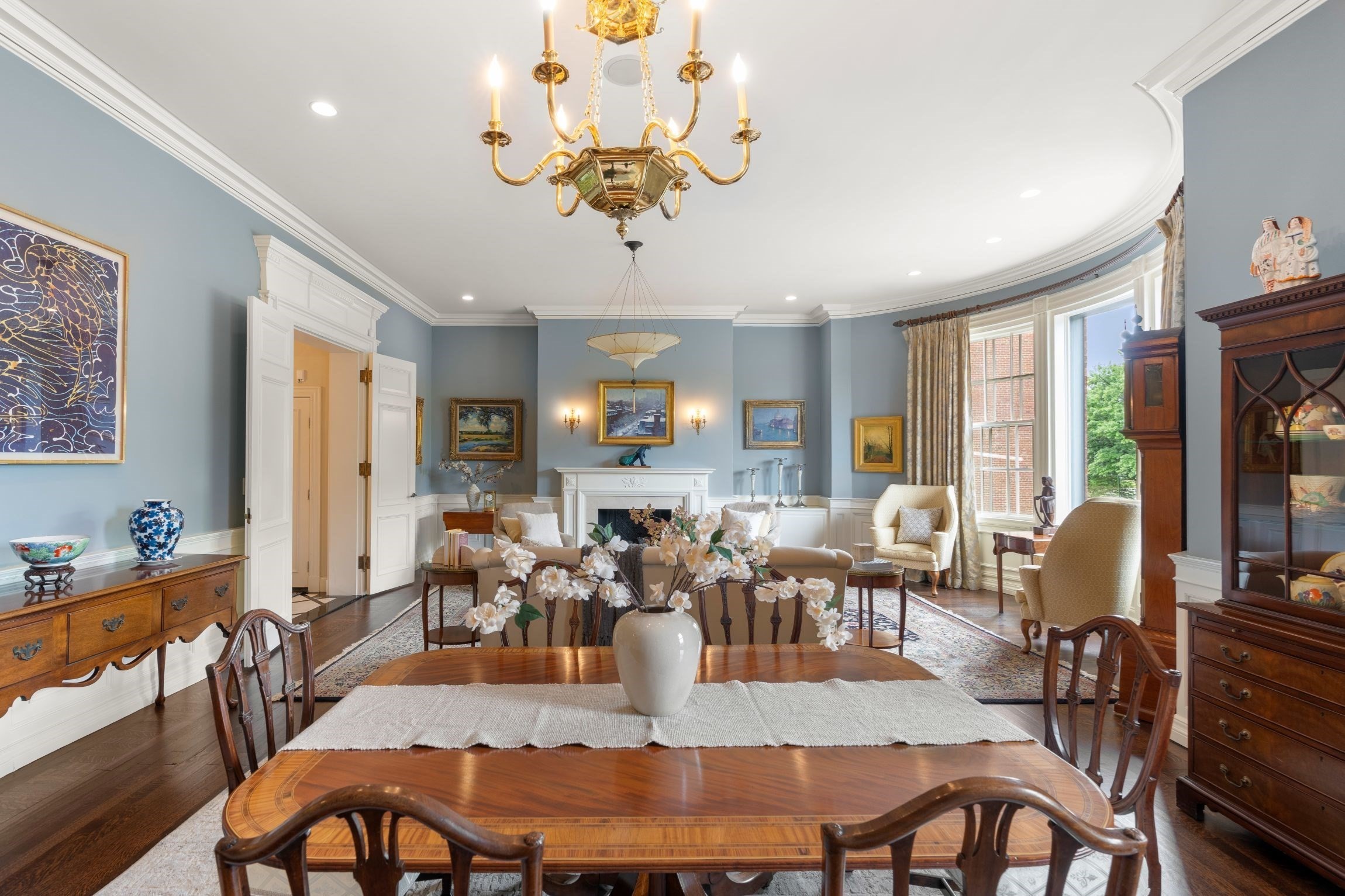 Formal living room with a white fireplace, blue walls, and chandelier; dining table in foreground.