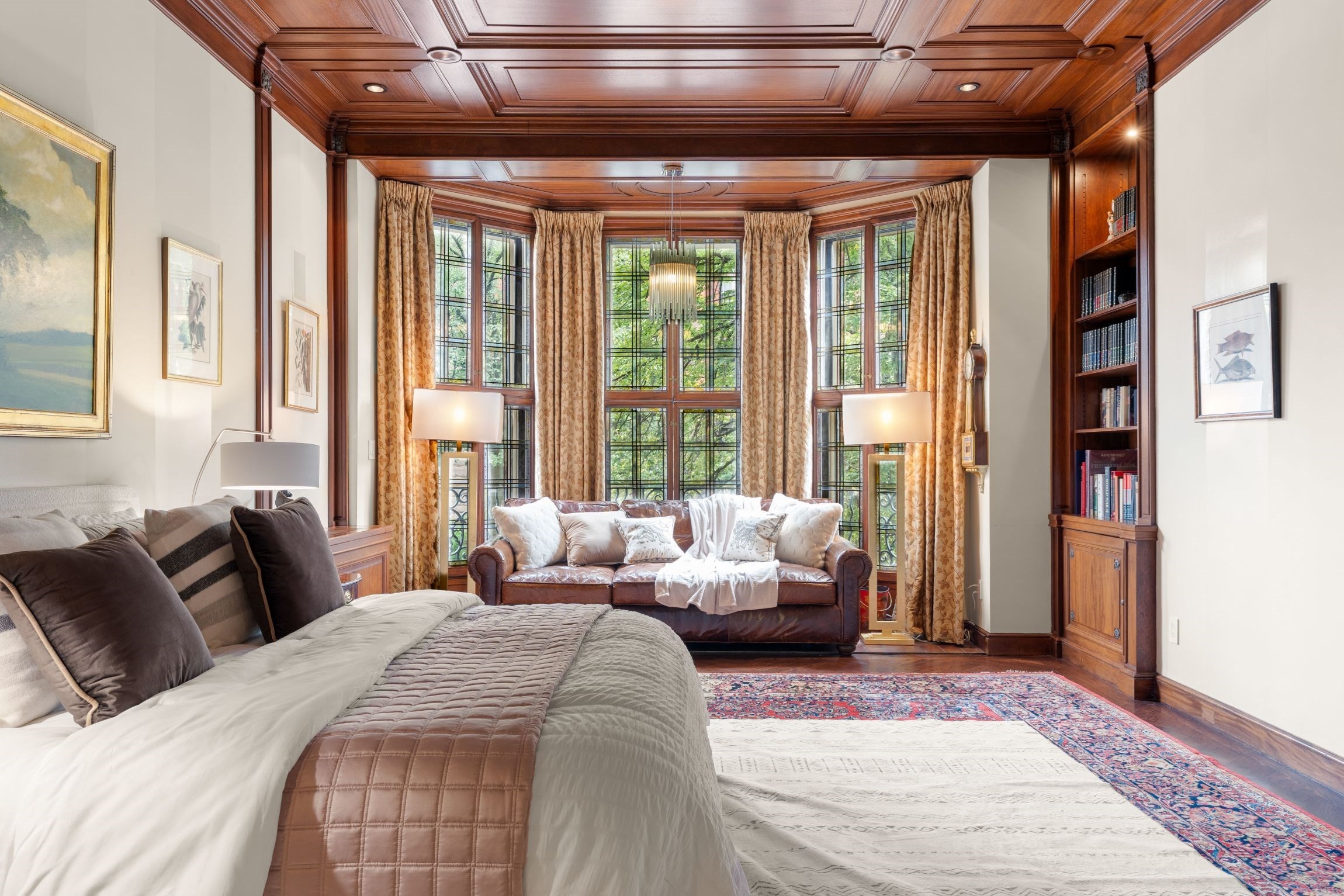 Bedroom with an ornate wood-paneled ceiling, tall curtained windows, and a sofa seating area.