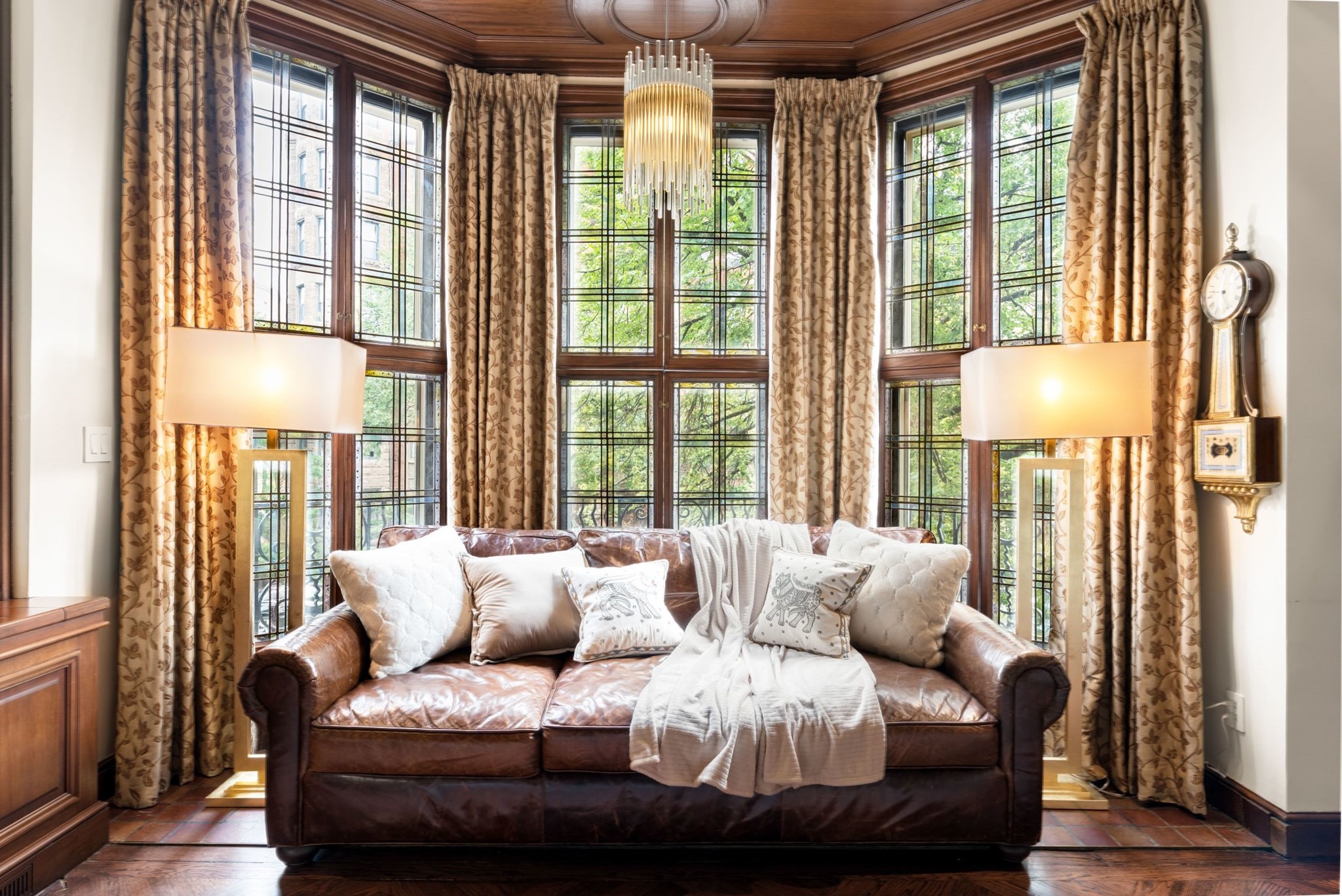 Living room with a leather sofa beneath tall leaded-glass windows and a wood-paneled ceiling.