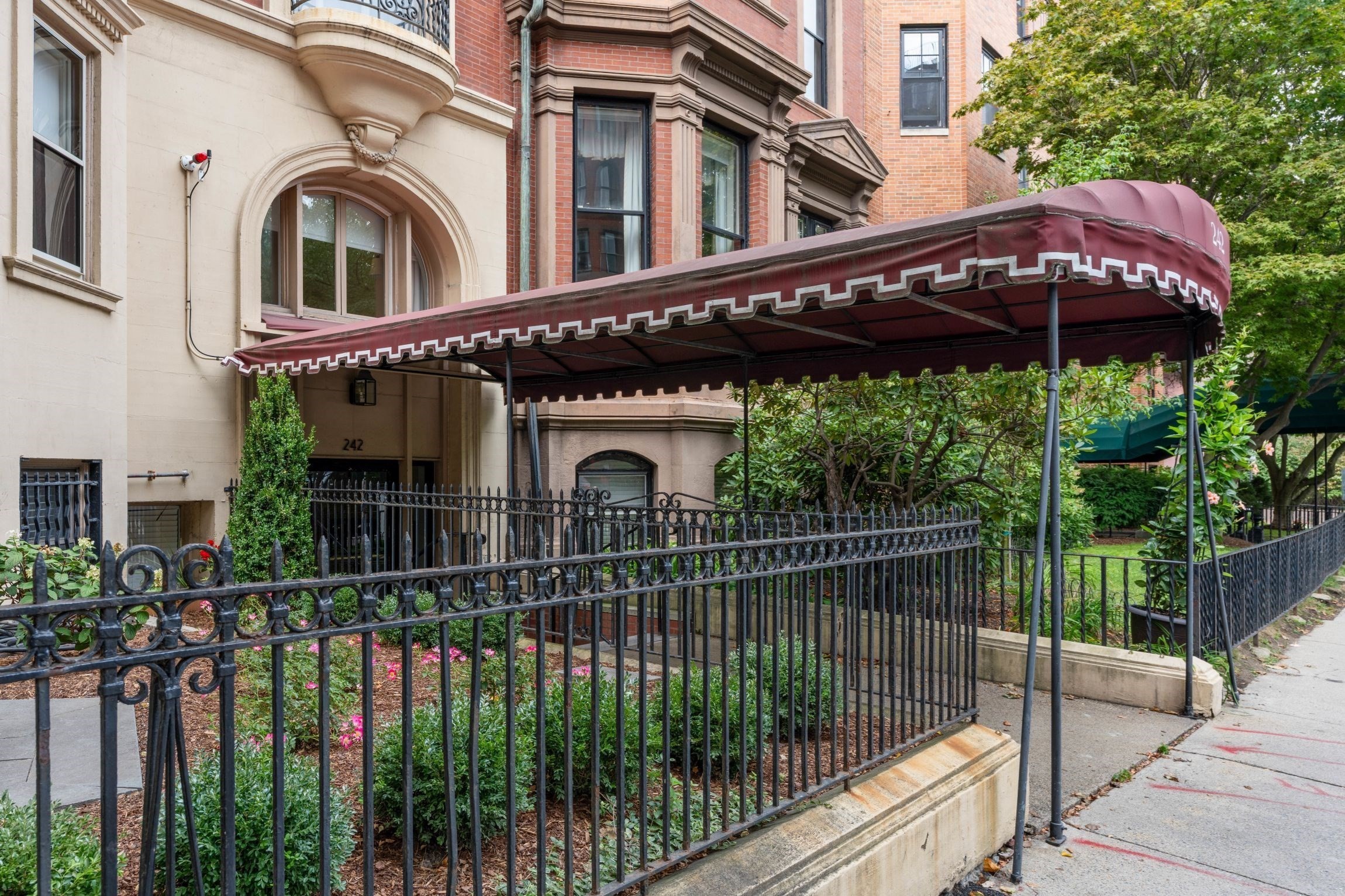 Building entrance with a burgundy canopy, arched doorway, and wrought-iron fence.