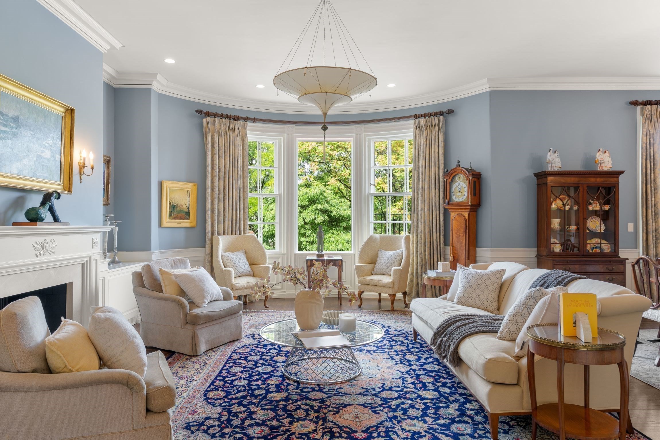 Furnished living room with bay windows, a white fireplace, and a richly patterned blue rug.