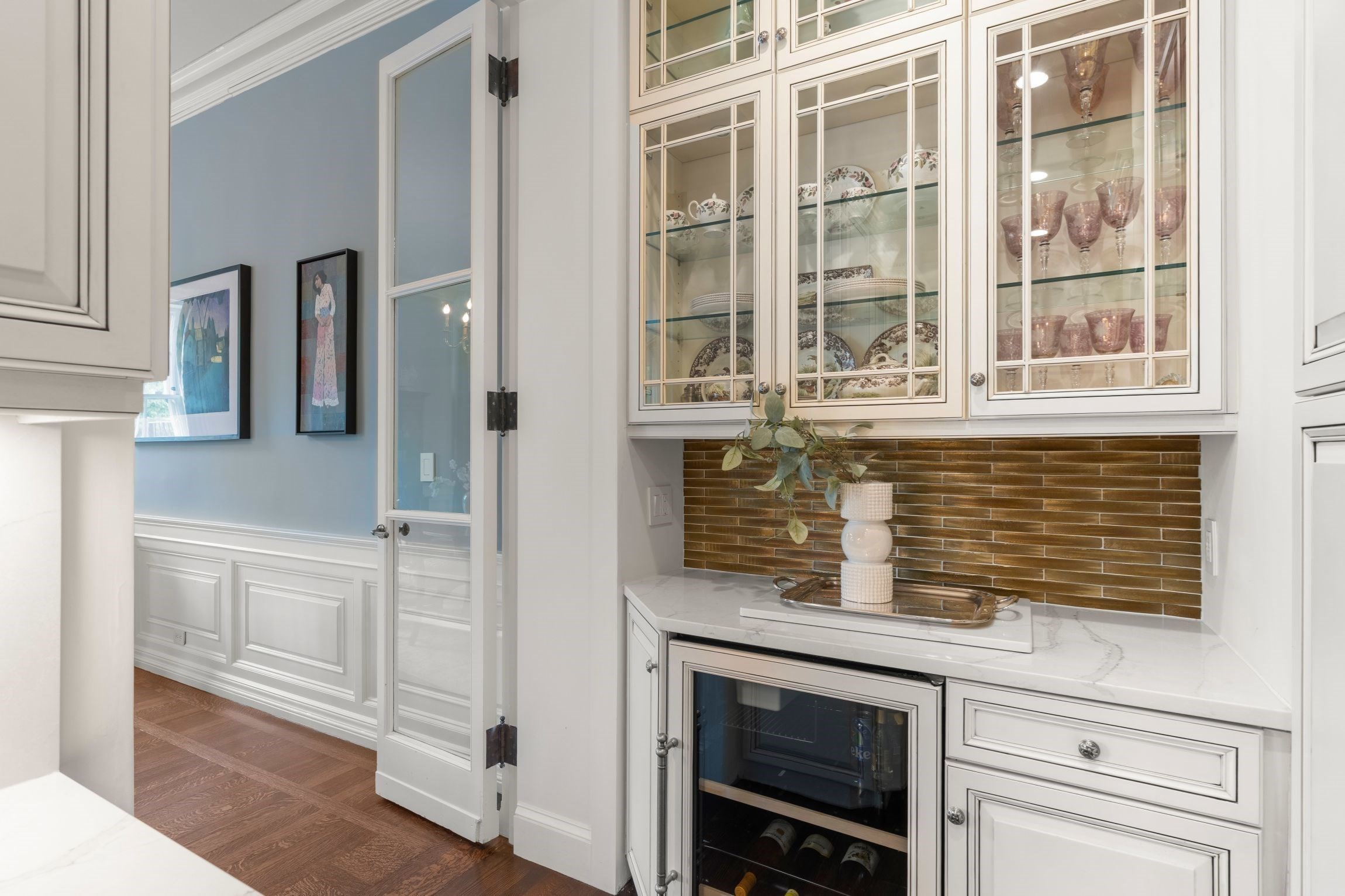 Kitchen wet bar with glass-front dish cabinets, brown tile backsplash, marble counter, and wine refrigerator.