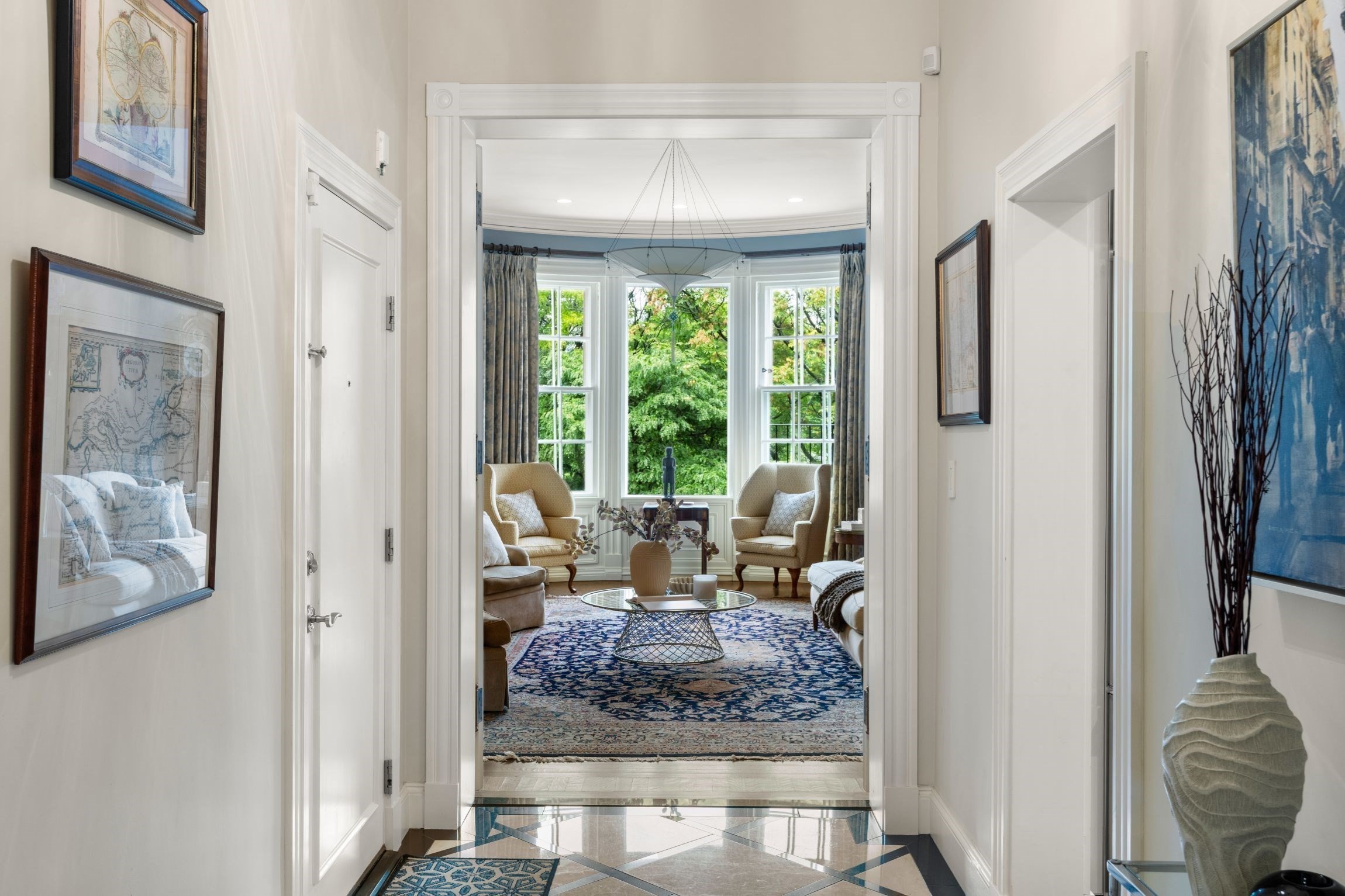 Furnished living room with a curved bay window, leafy views, and a patterned blue rug.