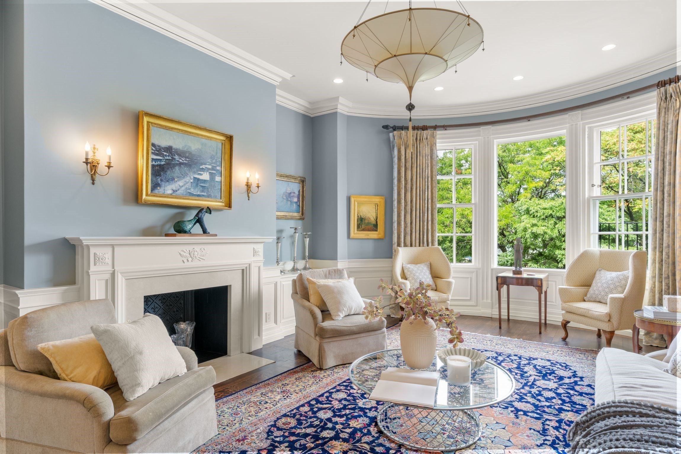 Living room with a white fireplace, bay windows, and a blue patterned rug.