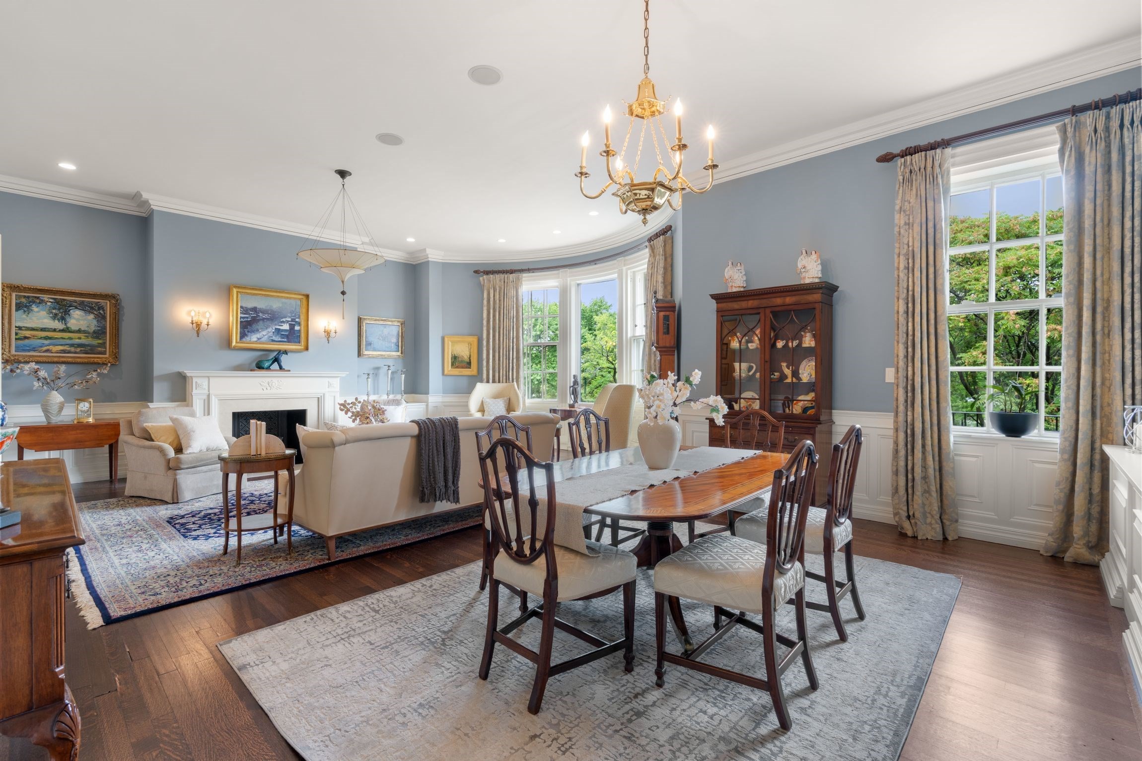 Living and dining room with a white fireplace, bay windows, and a polished wood dining table.